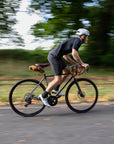 Model cycling on a bikepacking tour with three orange bicycle bags attached.