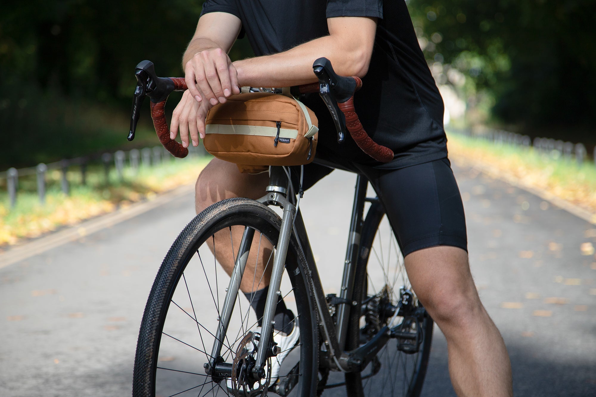 Model resting on orange cross body bicycle bag, rural setting. 