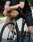 Model resting on orange cross body bicycle bag, rural setting. 