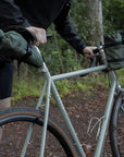 Model holding a touring bike with three green cycling bags attached, rural setting. 