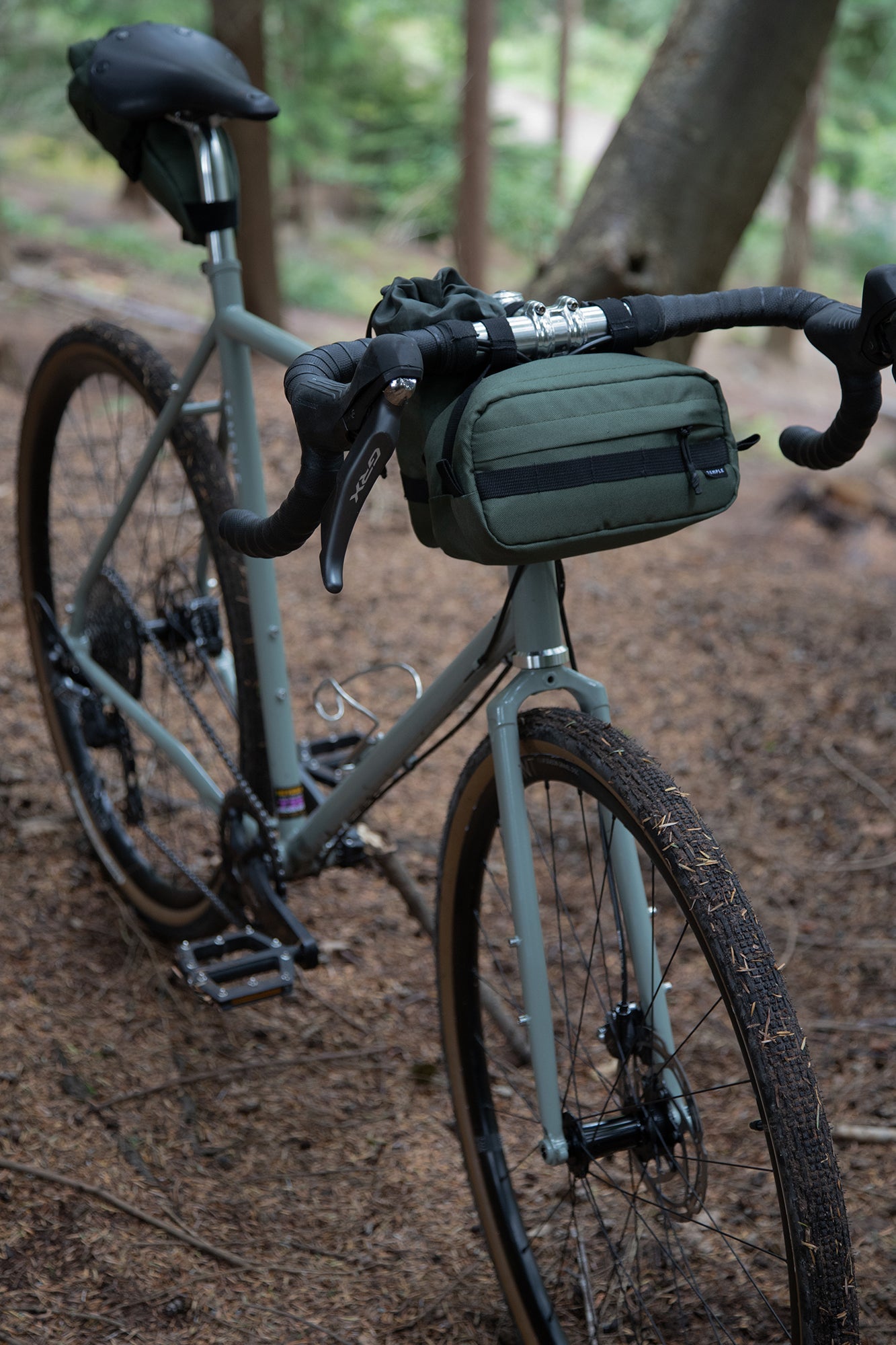 Bikepacking bag with Temple bar bag in green attached, forest setting.