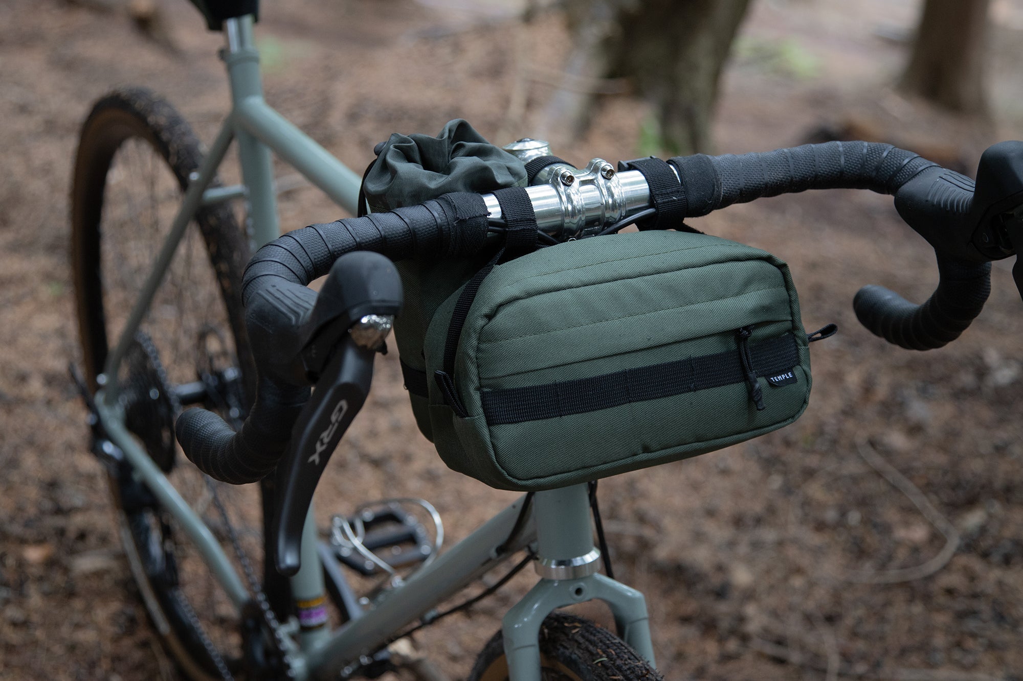 Olive green, waterproof bar bag attached to a road bike, forest setting.