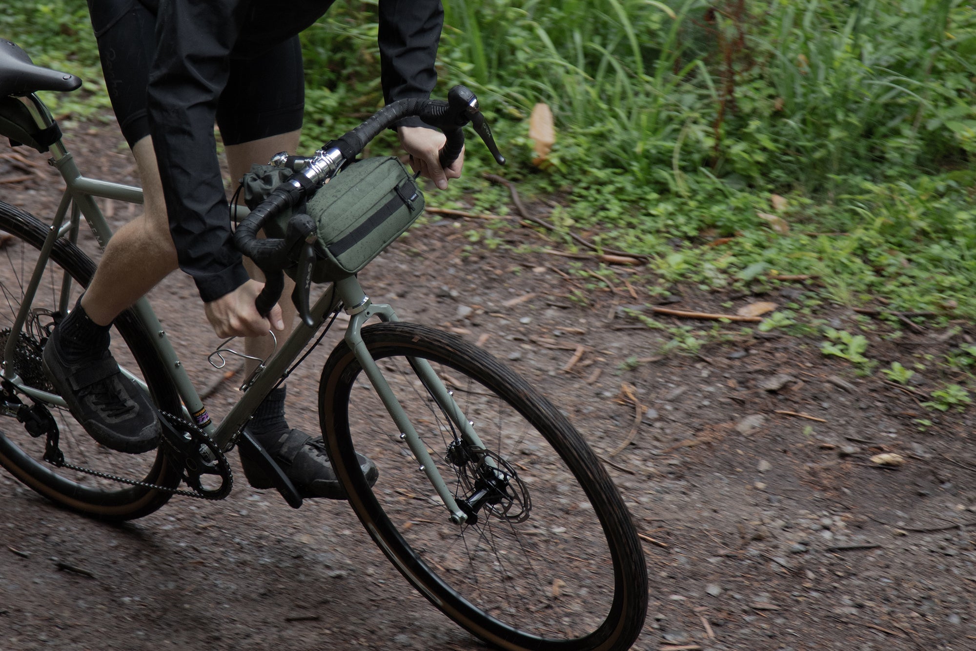 Bikepacking model cycling on a steel road bike with a green snack bag attached to the handlebars.