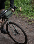 Bikepacking model cycling on a steel road bike with a green snack bag attached to the handlebars.