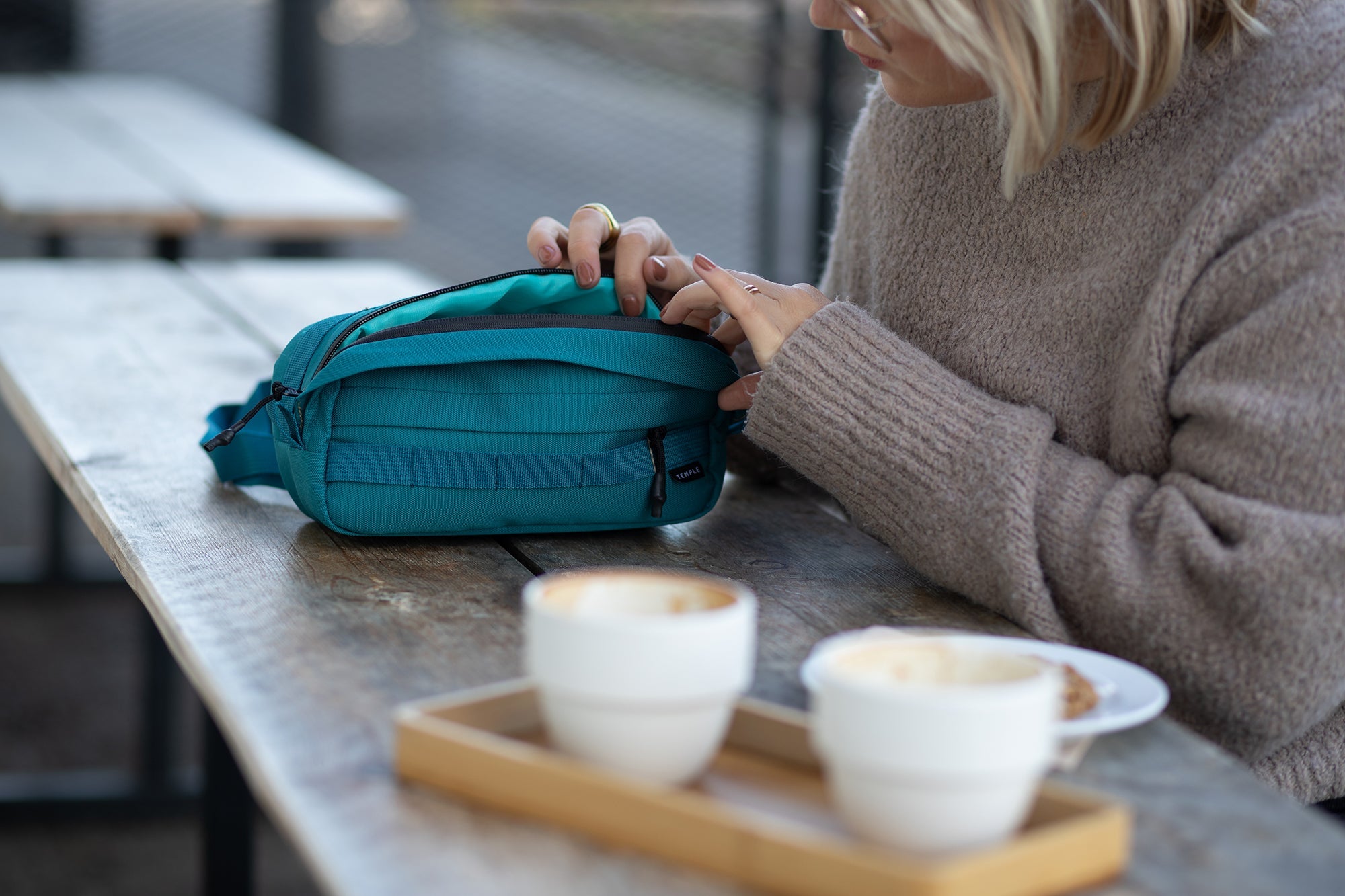 Model opening casual green bum bag in a café setting.