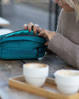 Model opening casual green bum bag in a café setting.