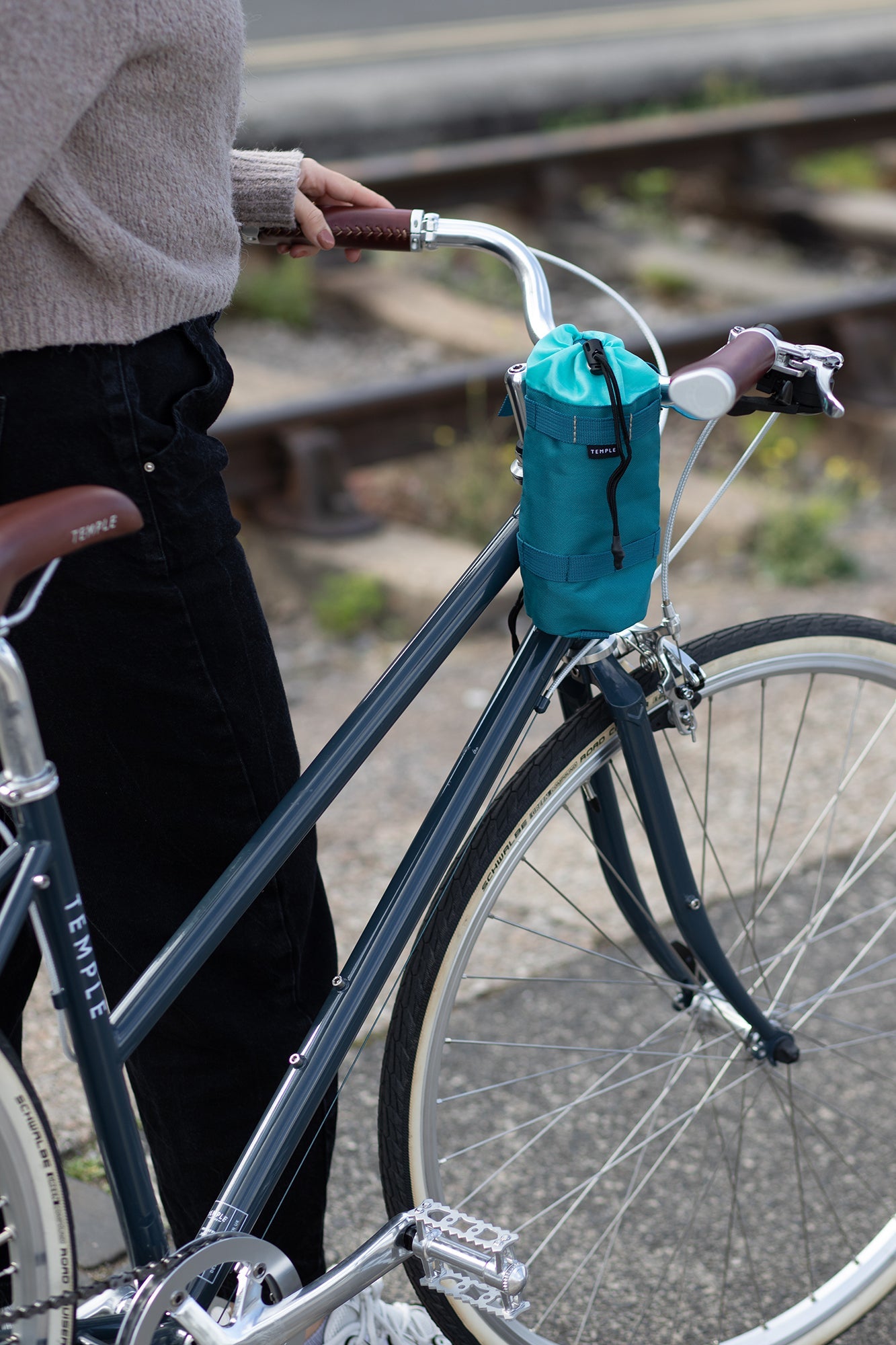 Model holding step through steel bike with a women’s green snack bag, urban setting. 