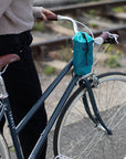 Model holding step through steel bike with a women’s green snack bag, urban setting. 