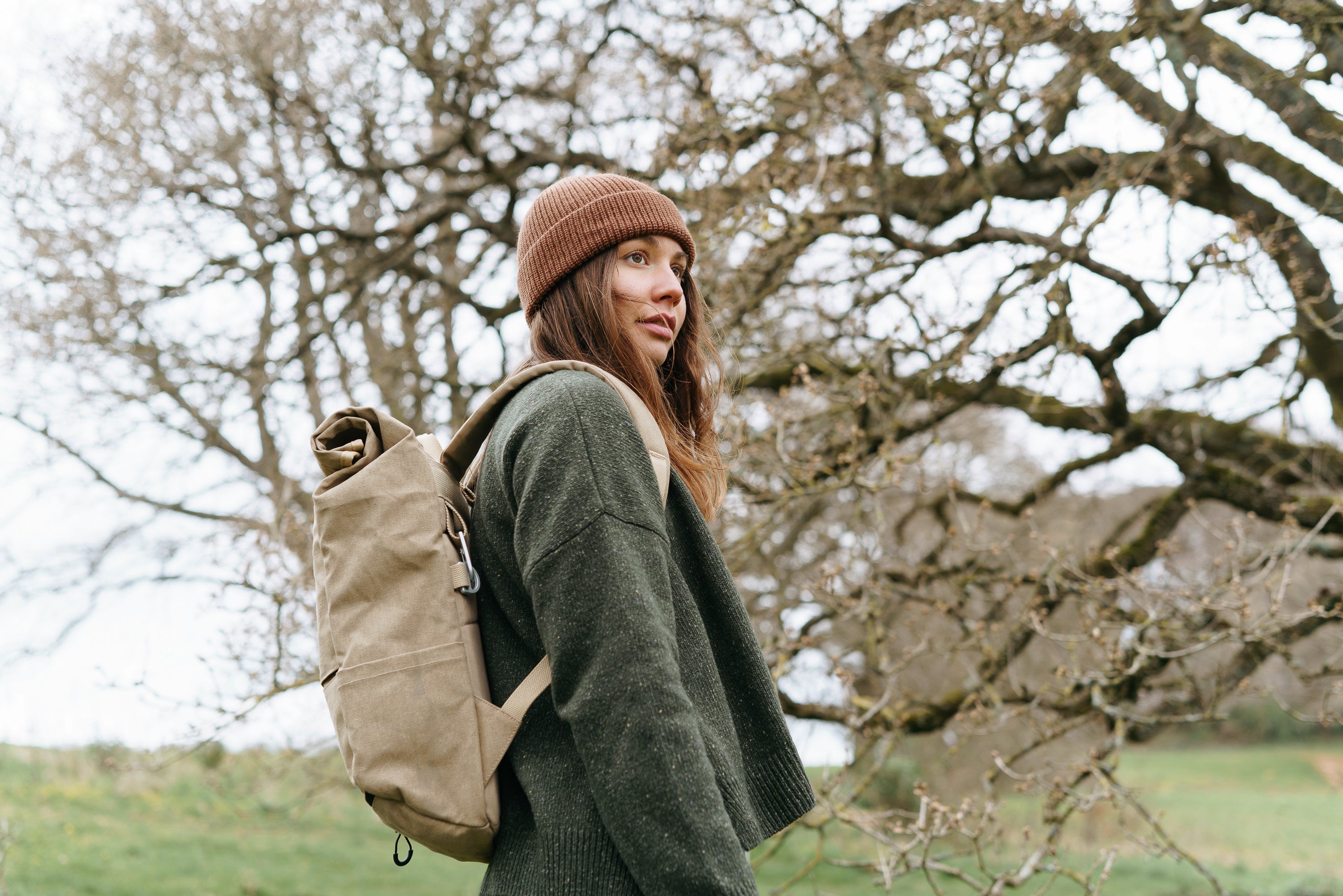 Model wearing a beige women’s backpack in a rural setting.