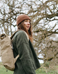 Model wearing a beige women’s backpack in a rural setting.