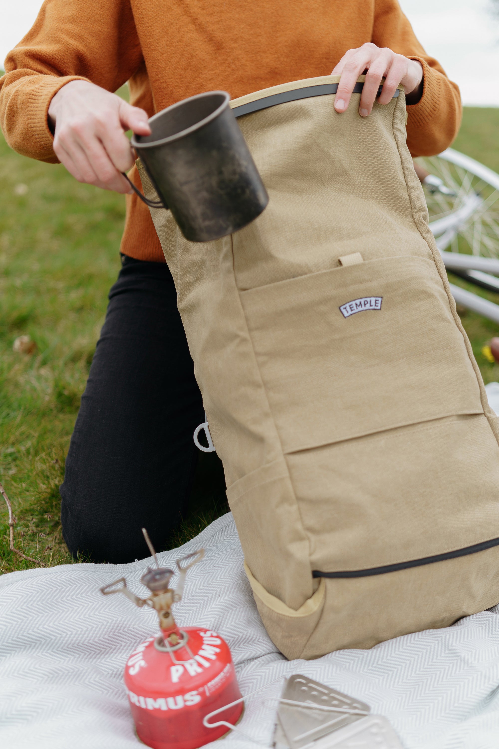 Model unpacking camping equipment from a roll top waterproof backpack, rural setting.