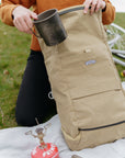 Model unpacking camping equipment from a roll top waterproof backpack, rural setting.