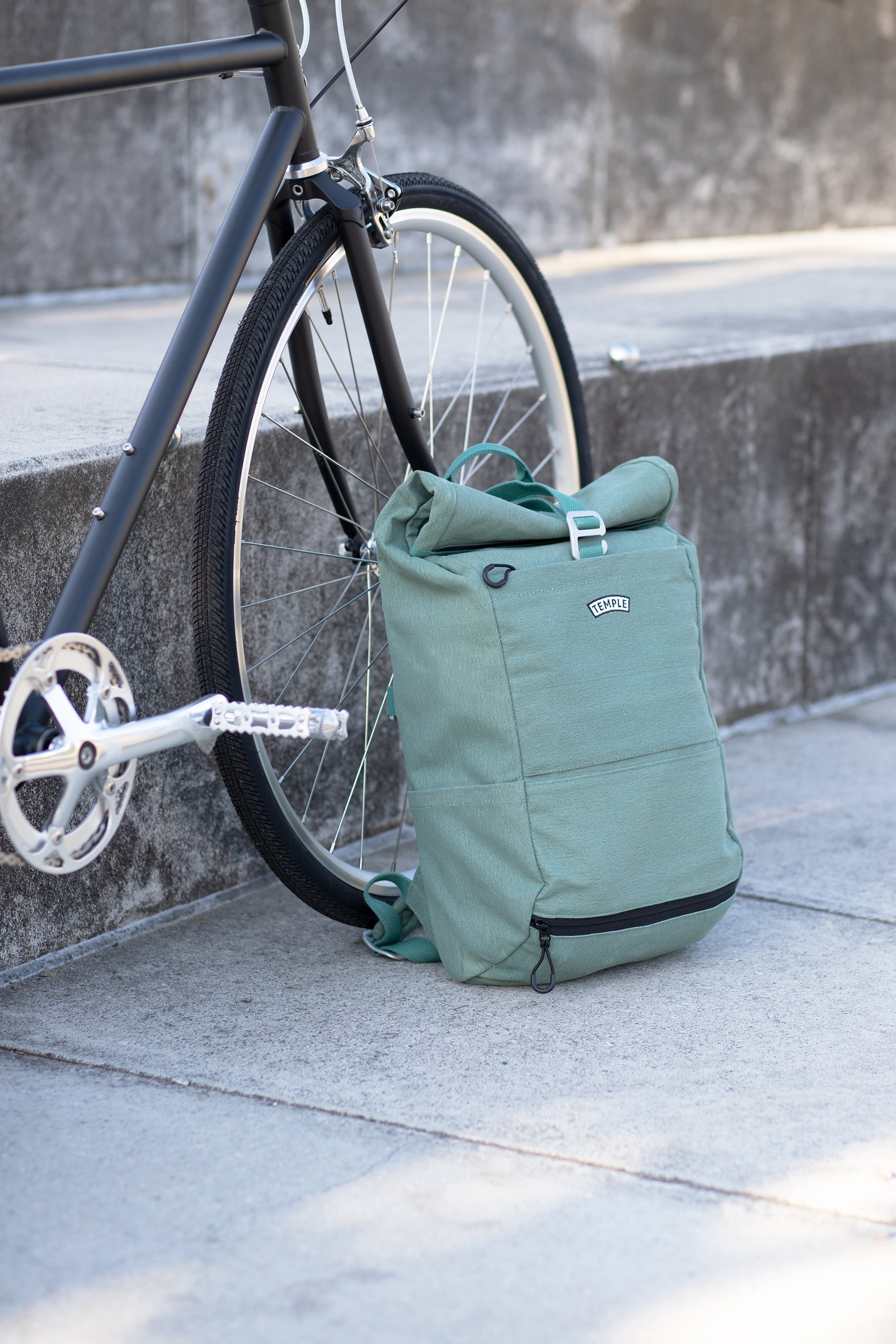 Green cycling backpack leaning against front bike wheel, urban setting.