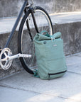 Green cycling backpack leaning against front bike wheel, urban setting.