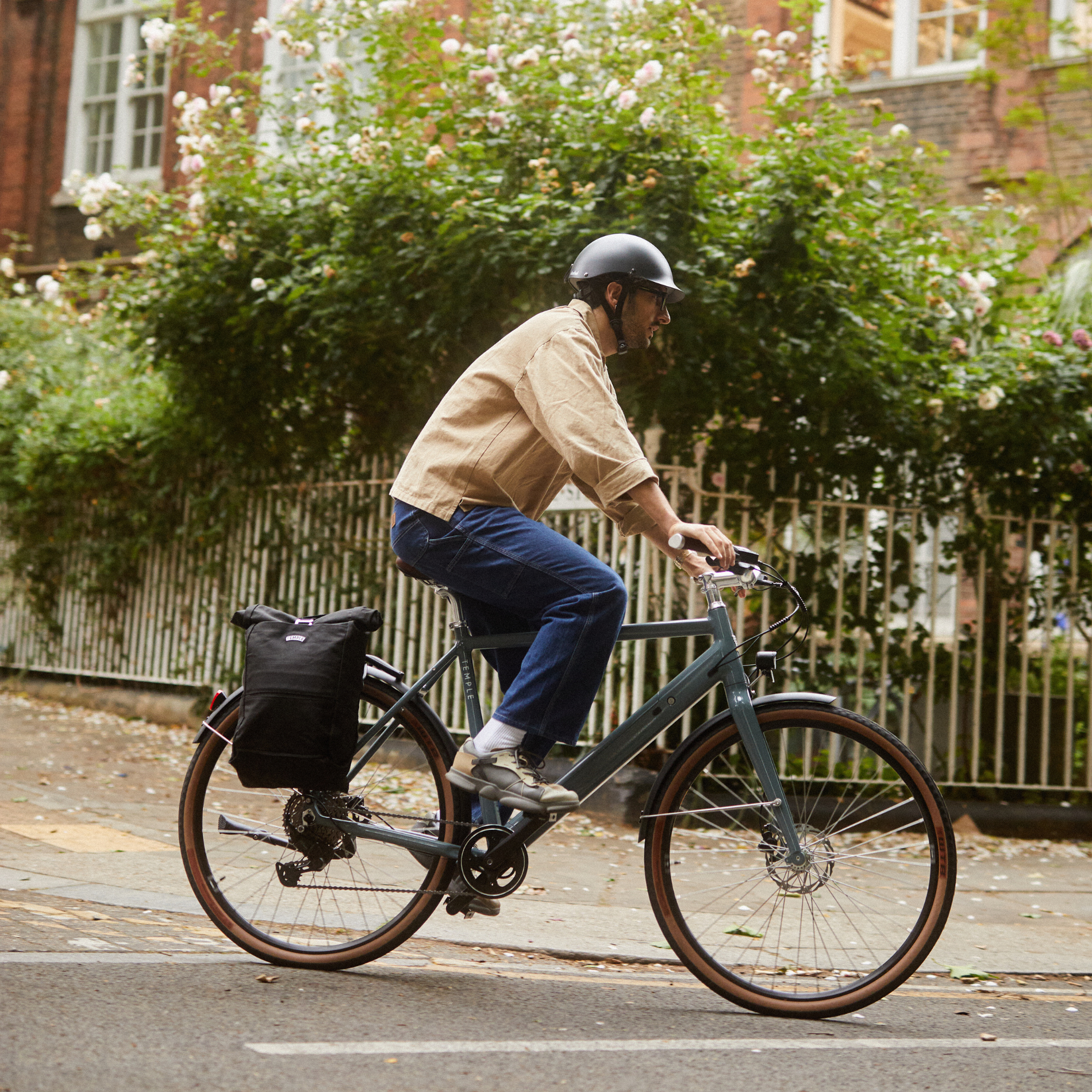 Man riding a bicycle on a city street with a building and greenery in the background