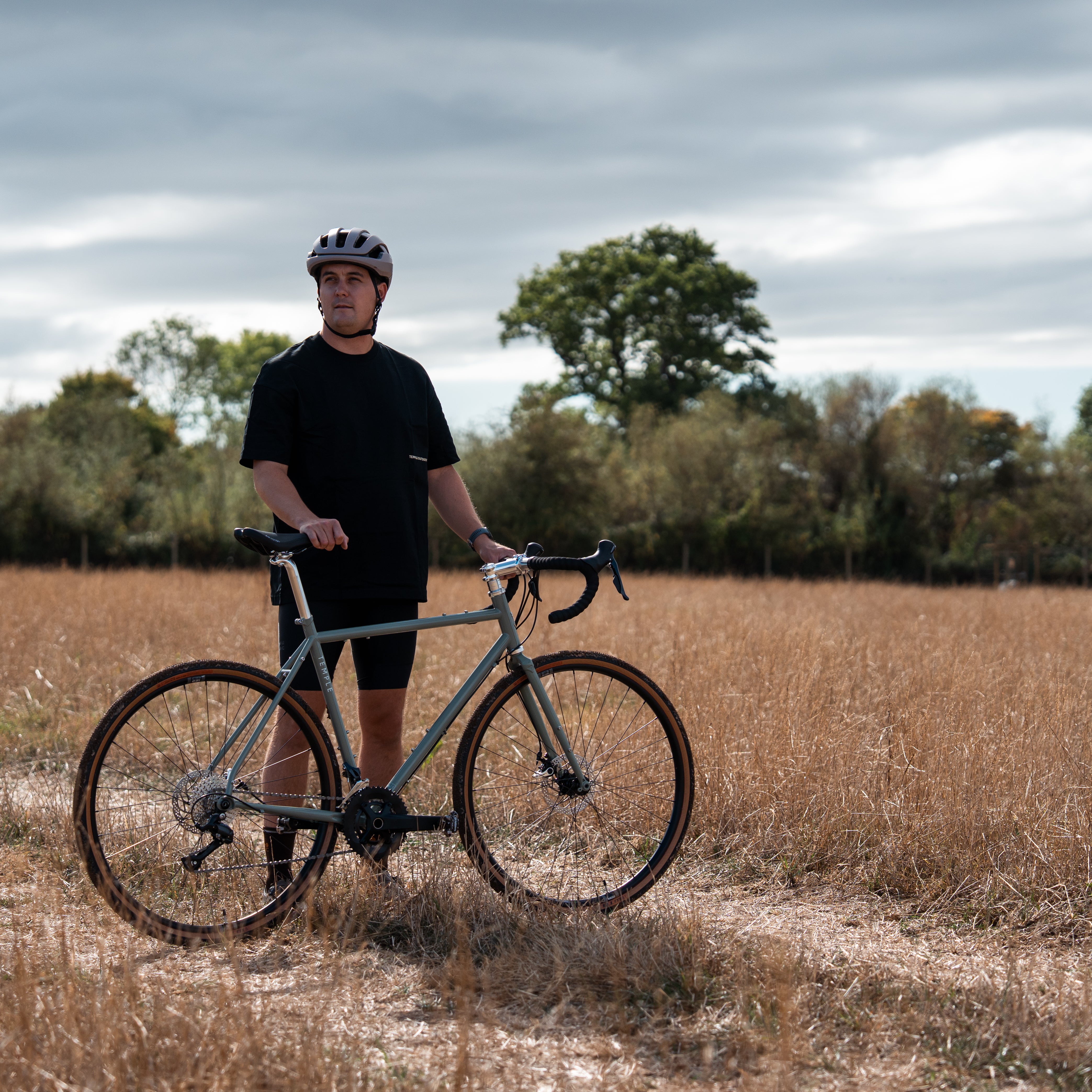 Man standing with a bicycle in a field on a cloudy day
