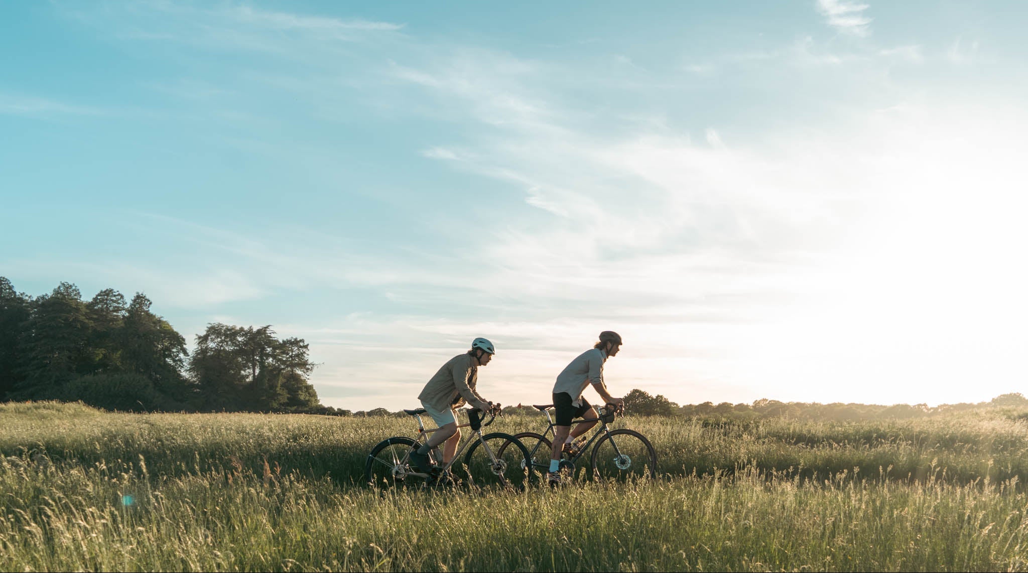 Two people riding bicycles in a grassy field with a clear blue sky.