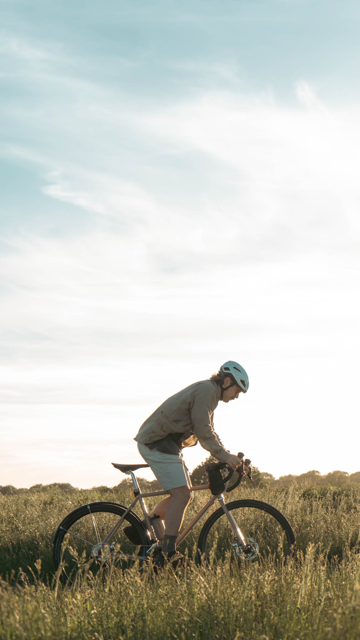 Two people riding bicycles in a grassy field with a clear blue sky.
