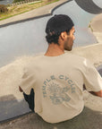 Back view of model wearing supper soft cream and green men’s graphic tee, skate park setting.