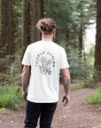 Men’s white graphic tee on model in forest setting.