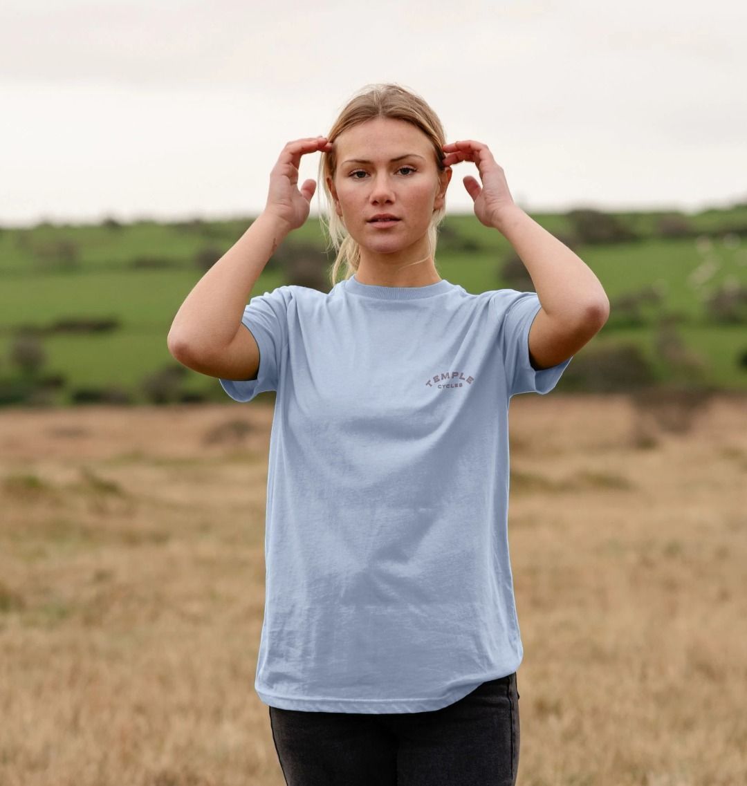 Women’s sustainable graphic t-shirt in light blue on model, rural setting.