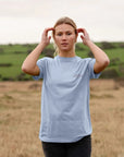 Women’s sustainable graphic t-shirt in light blue on model, rural setting.