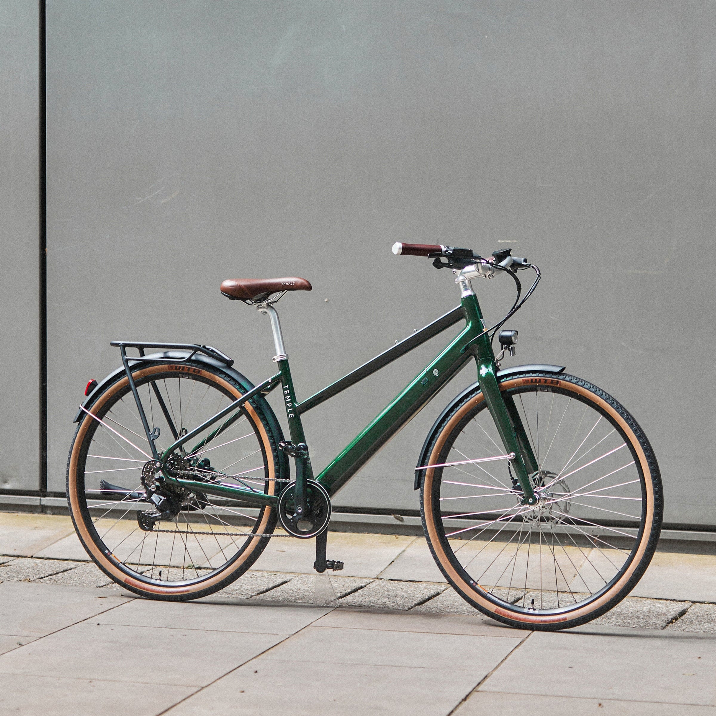 Green bicycle parked on a sidewalk against a gray wall