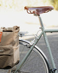 Beige pannier backpack on lightweight steel touring bicycle in a rural setting.