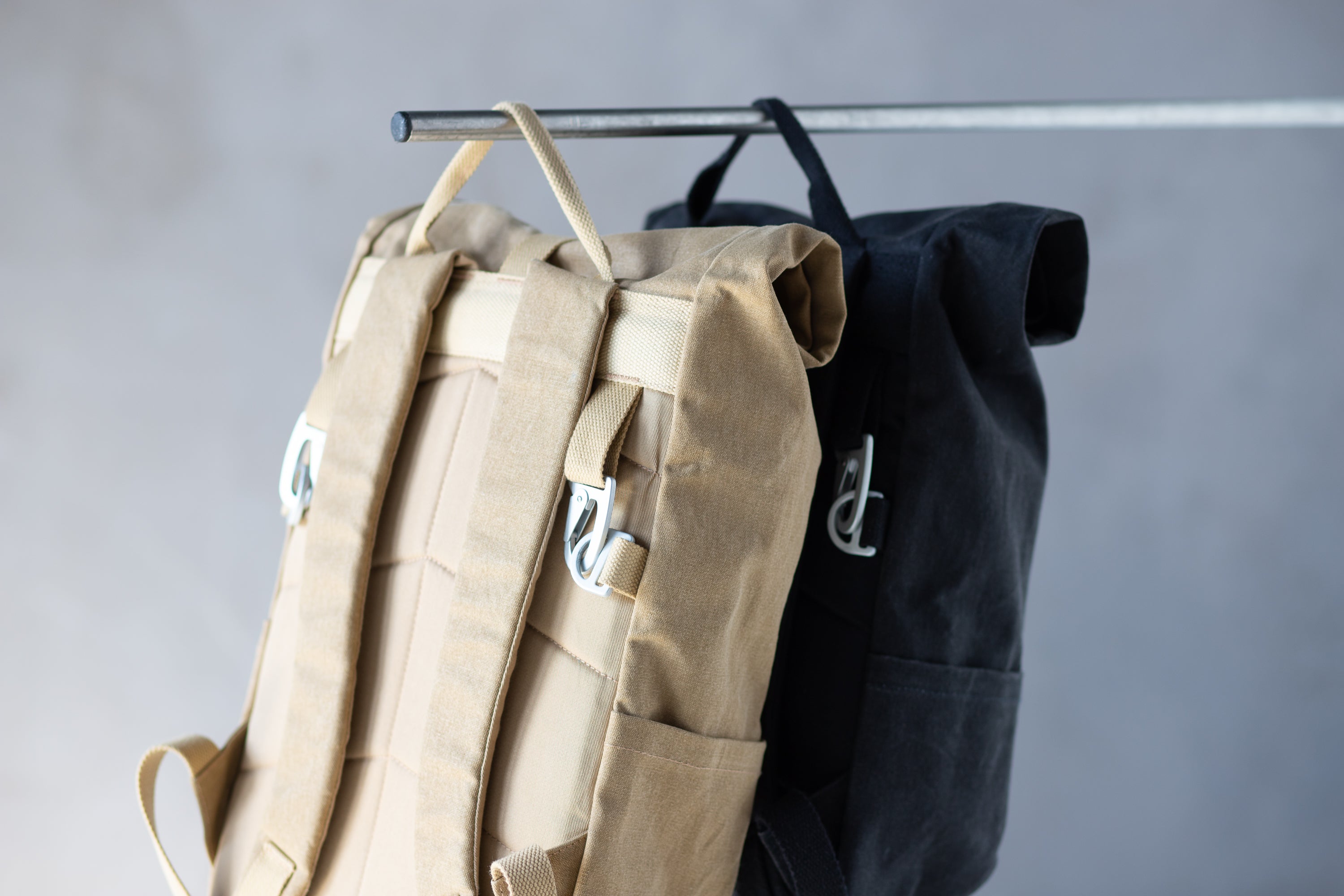 Shoulder strap view of two waterproof pannier backpacks with aluminium clips, studio setting.