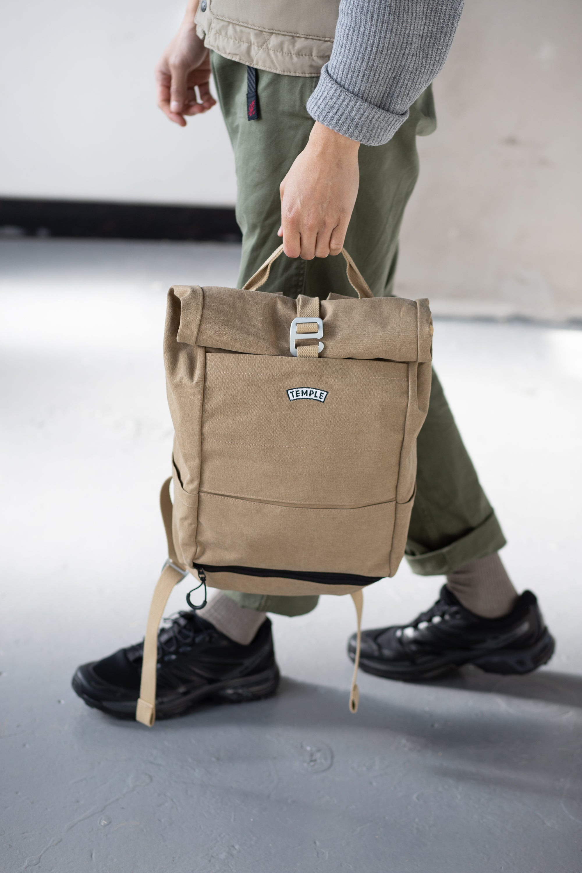 Man holding a waterproof roll-top rucksack in beige, urban setting. 