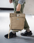 Man holding a waterproof roll-top rucksack in beige, urban setting. 