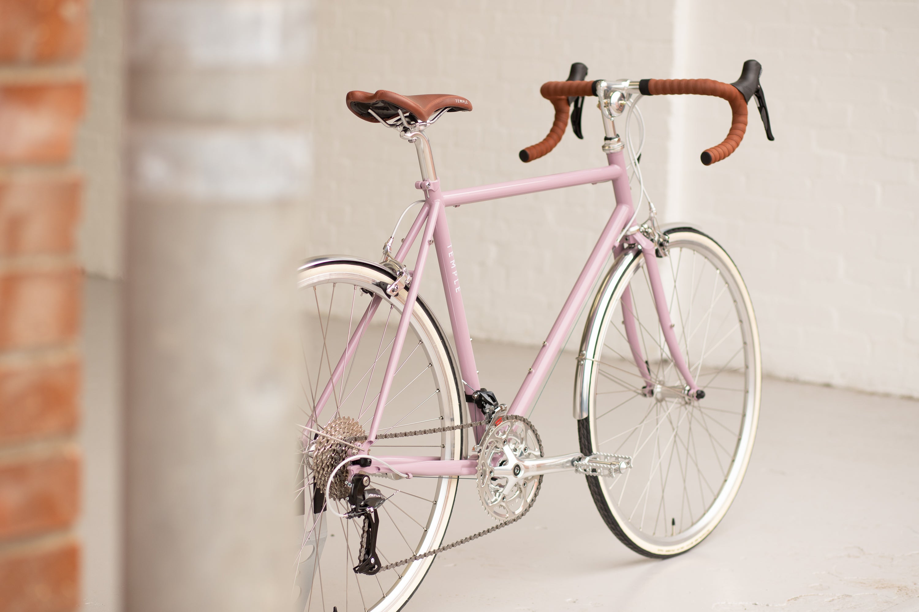 Pink lightweight touring bicycle with drop handlebars in a studio setting.