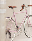 Pink lightweight touring bicycle with drop handlebars in a studio setting.