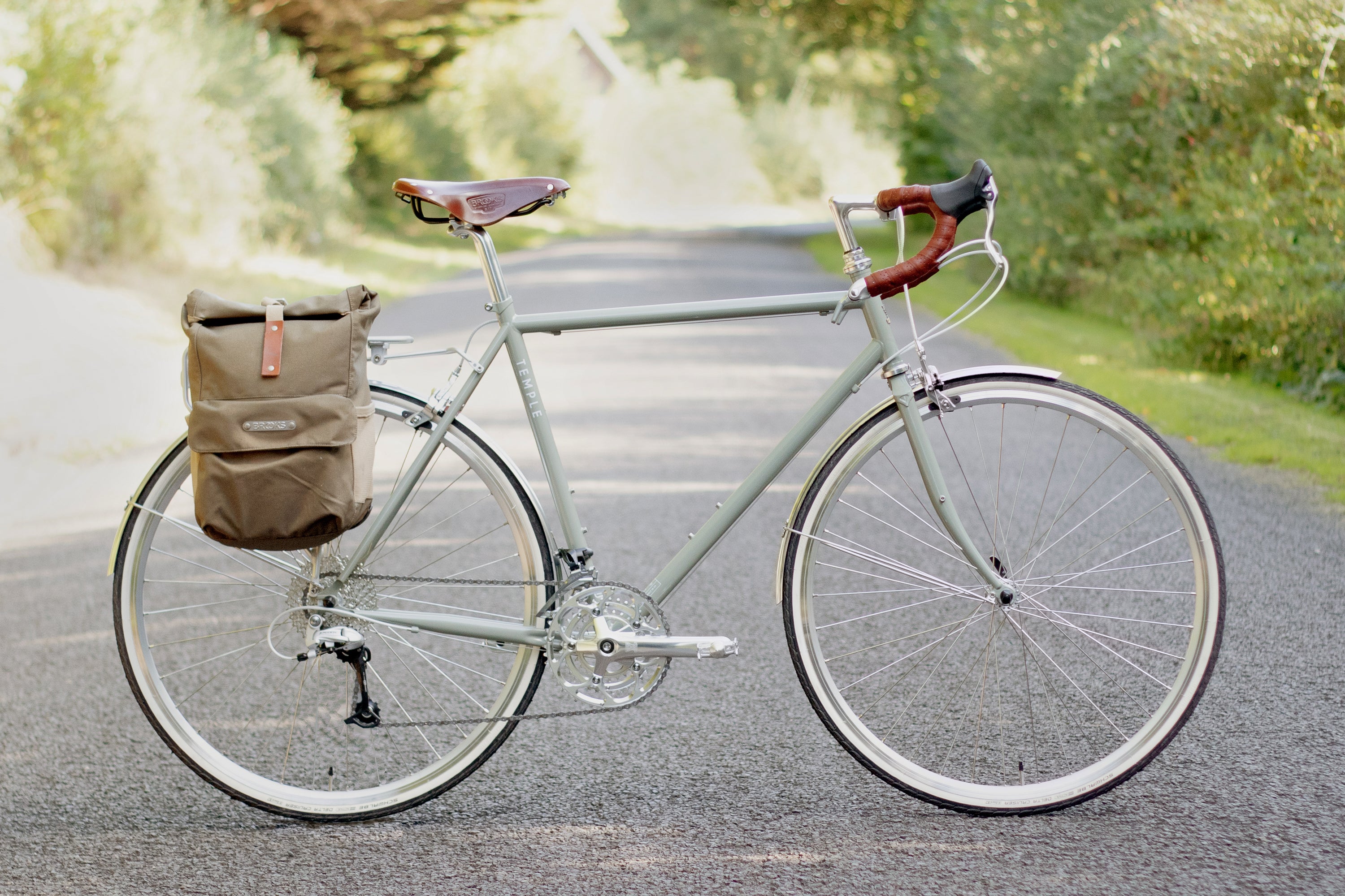 Green touring bike with pannier backpack in a rural setting.